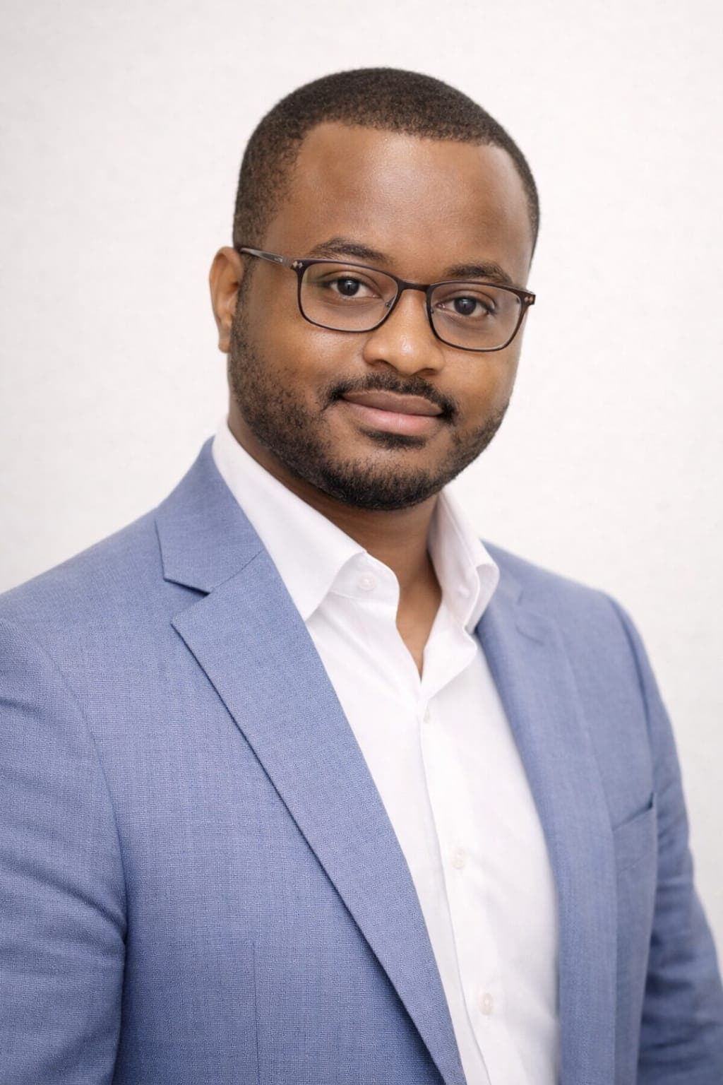 Black man with glasses and a beard wearing a light blue blazer and white shirt.